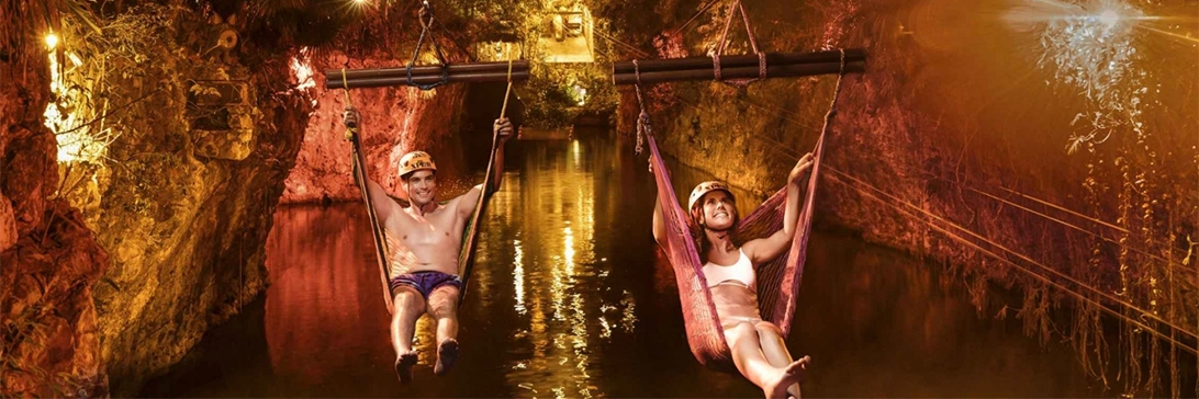 Siblings speed toward a river below, each in their own zip-linning hammock