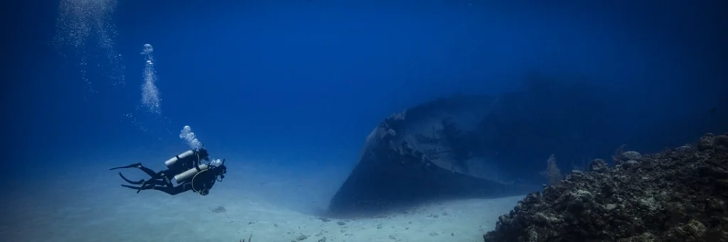 Two divers swim towards a shipwreck